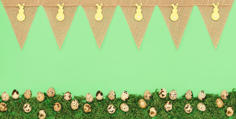 Green background with a burlap banner with Easter bunny cutouts and row of speckled eggs