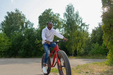 A happy African American man rides a bicycle through a public park. Healthy lifestyle.