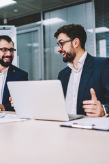 Two office workers in business meeting sitting at desk using computer for business training, professionals smiling and using modern electronics devices during conversation about successful project