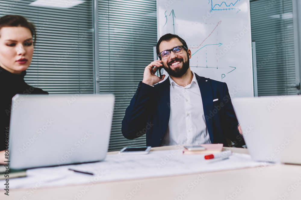 Poster successful male executive manager in eyeglasses having mobile conversation in funny atmosphere on mo