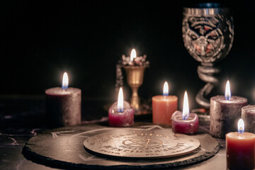 An eerie occult ritual setup featuring lit candles, a mystical symbol on slate, and a ceremonial...