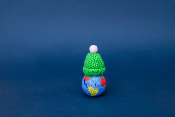  A model of the earth on a dark background in a woolen hat.  Concept of Earth day, organic gardening, ecology, sustainable life.