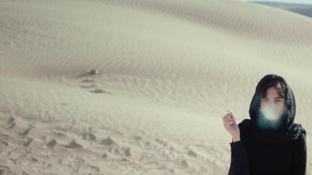 Woman in hijab in the desert smoking a cigarette