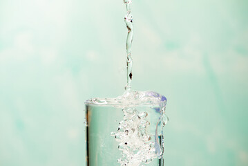 Splash in a glass, drop of water falling into a transparent glass, light background, selective focus