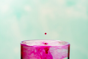 Splash in a glass, drop of violet liquid falling into a transparent glass, light background,...