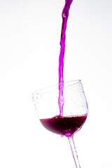 Splash in the glass, transparent glass receiving violet liquid, white background, selective focus