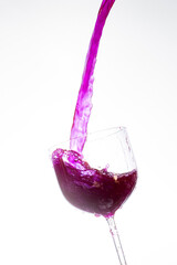 Splash in the glass, transparent glass receiving violet liquid, white background, selective focus