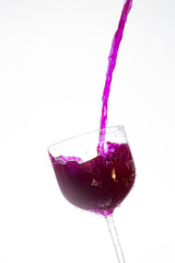 Splash in the glass, transparent glass receiving violet liquid, white background, selective focus