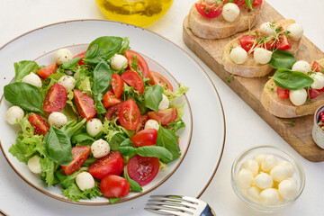 Salad with mozzarella, cherry tomatoes and green lettuce in a white round plate on the table