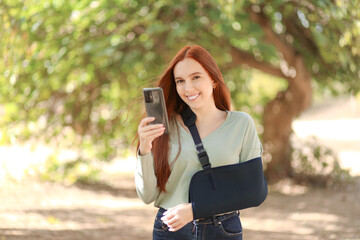 Attractive redhead woman with one arm in a sling smiles while holding her smartphone