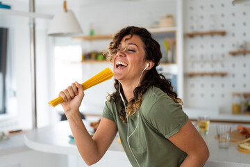 Closeup of young ecstatic woman with pasta straps singing and listening music on phone in kitchen.
