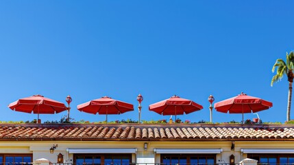 Bright red umbrellas adorn the rooftop against a stark blue sky, creating a striking contrast above a Spanish-style building