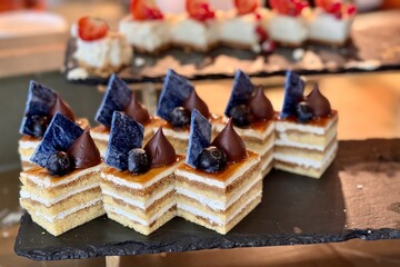 The portions of layered cream cake with blueberry on a black stand on the counter of the restaurant. Close-up