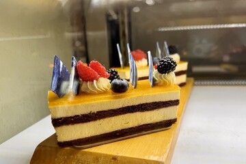 A portion of layered cream yellow cake with red raspberries, blackberries, blueberries on a wooden stand on the counter of the restaurant. Close-up