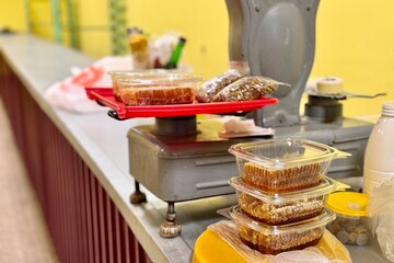 Honeycombs with honey in transparent plastic containers on the counter for sale lie next to the scales. Wax structures made of honey in the food market