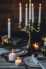 Beautiful table setting for family Christmas dinner at home. Cozy atmosphere, candlelight. Wine glasses, vintage chandelier, elegant interior. Fir tree branches, wooden furniture, dark, bokeh