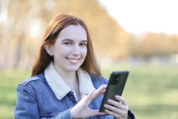 Beautiful smiling woman uses her phone while walking in the park