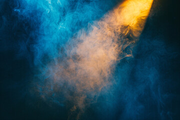 Royal blue smoke wafts over a stage under a sun-yellow spotlight, casting a warm glow against a deep navy background.