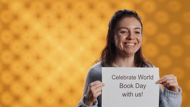 Portrait of happy woman holding placard with world book day message written on it, isolated over studio background. Geek promoting importance of reading during 23th April global event, camera A - Powered by Adobe