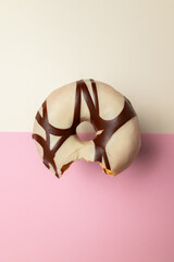 A chocolate and white donut with a bite taken out of it. The donut is sitting on a pink background
