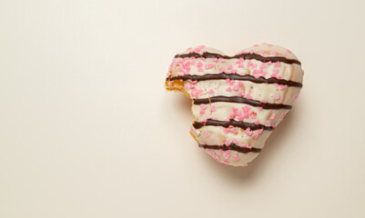 A heart-shaped donut with pink and brown frosting. The donut is half eaten, with a bite taken out...