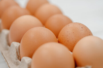 orange hen eggs lying in cardboard box, dozen eggs on white wooden background, selective focus