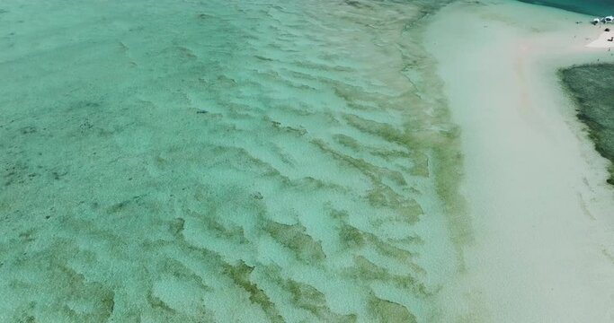 Turquoise sea water with white sand ocean floor. Sandbar with boats and waves. Surigao del Sur, Philippines.