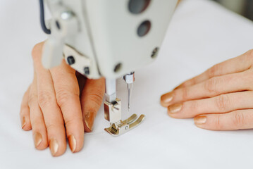 sewing machine with needle and thread on table in atelier, close-up view of hands of working...
