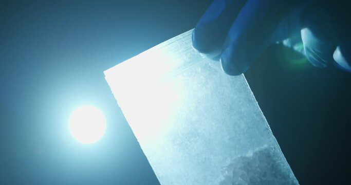 Police Evidence Examination. Police Detective Examining Meth or Cocaine at Crime Scene in Hand. Using Flash Light on Baggy of Drugs, Meth, Close