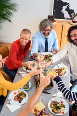 Vertical Top view of Caucasian family at a meal together at home toasting with white wine and drinking at table. Happy people gathered to enjoy festive event. Different generations and domestic life