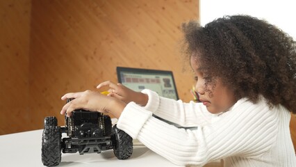 Smart african girl build robotic car while using wires while using laptop setting or writing prompt code. Skilled female student working on computer in STEM technology online classroom. Erudition.