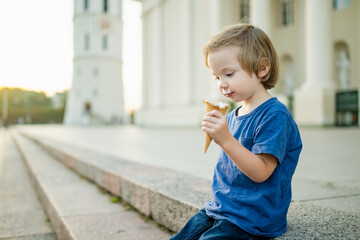 Cute little boy eating tasty fresh ice cream outdoors on warm sunny summer day in Vilnius, Lithuania.