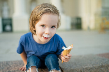 Cute little boy eating tasty fresh ice cream outdoors on warm sunny summer day in Vilnius, Lithuania.