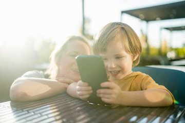 Cute toddler boy playing with a phone in outdoor cafe.