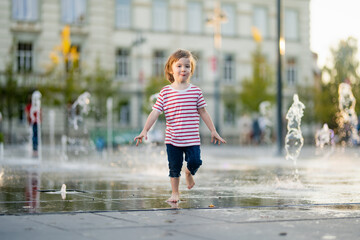 Cute little boy having fun with water in city fountain. Child playing water games outdoors on hot day. Summer activities for children.