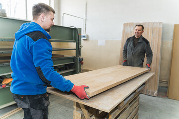 two craftsmen holding a wooden panel at the workshop, belt grinder machine. High quality photo