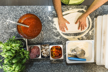 chef surrounded by ingredients shaping the dough to make pizza, top down view. High quality photo