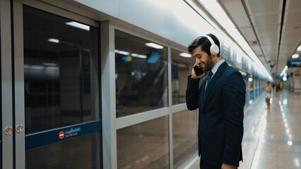 Smart business man calling phone while wearing headphone at train station. Professional executive...