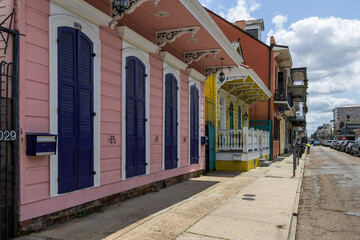 Homes and parked cars along a street in the french quarter with people walking, flags, blue sky and clouds in New Orleans Louisiana USA