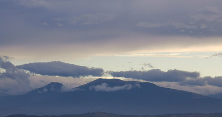 Nuvole bianche e grigie aggrappate come ovatta alle montagne in una giornata invernale al tramonto