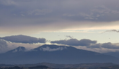 Nuvole bianche e grigie aggrappate come ovatta alle montagne in una giornata invernale al tramonto