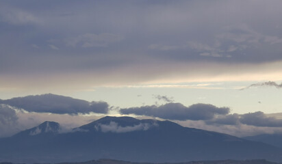 Obraz premium Nuvole bianche e grigie aggrappate come ovatta alle montagne in una giornata invernale al tramonto