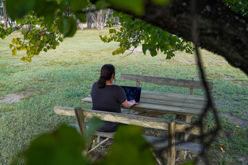 Fototapeta premium Woman working remotely on a wooden bench under a tree