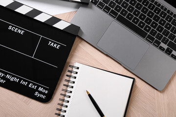 Movie clapper, notebook, laptop and pen on wooden table, flat lay