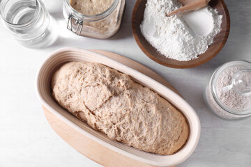 Fresh sourdough in proofing basket, flour and water on light table, flat lay