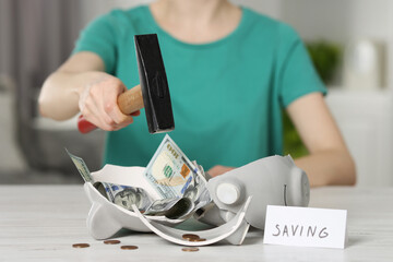 Financial savings. Woman breaking piggy bank with hammer at table indoors, closeup