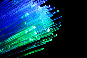 Optical fiber strands transmitting green and blue light on black background, macro view