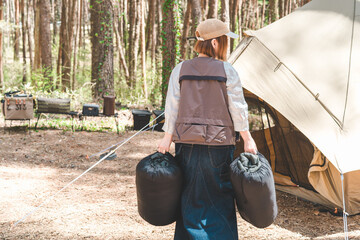 キャンプ場で寝袋・シュラフを運びテント設営をする女性キャンパー
