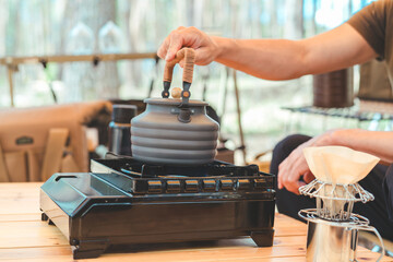 キャンプでコンロとケトルを使ってお湯を沸かしコーヒーを淹れる男性キャンパーの手元
