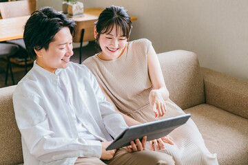 マイホームでソファに座りながらタブレットを見る若いアジア人夫婦（くつろぐ・カップル・仲良し）
